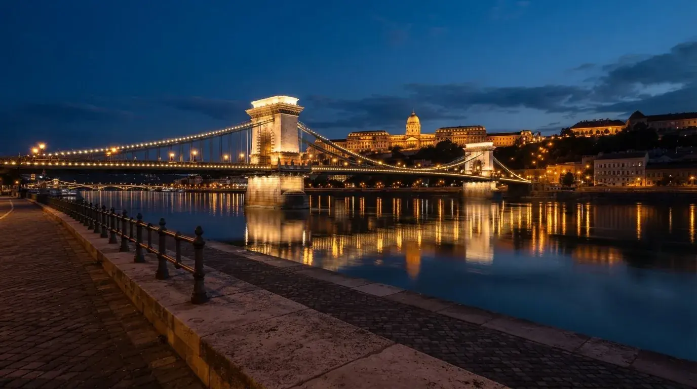 A budapesti Lánchíd esti fényekben a Duna fölött, a háttérben a budai Vár, forgalom nélküli rakpart.